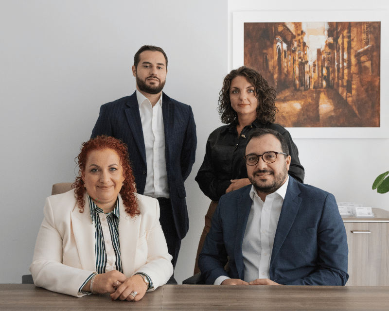 A2CO's Tax team including Partner Antoinette Scerri, Benjamin Zammit McKeon, Stephanie Bianco and Clivert Vella posing for a photo with two of them standing.