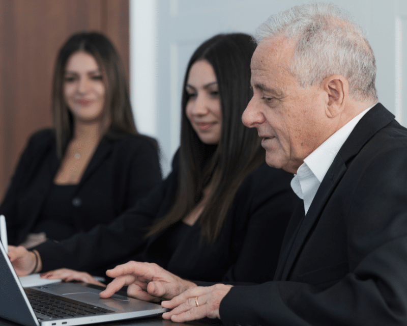 A2CO's Accounts Department posing for a photo in the board room, including Cliona Testa Refalo, Chanel Borg and Joe Sacco while looking at a laptop.