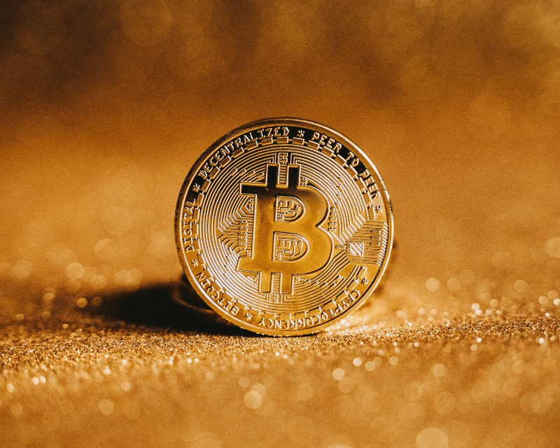 Close-up of a golden Bitcoin standing upright on a glittering golden surface, symbolising cryptocurrency and digital assets.