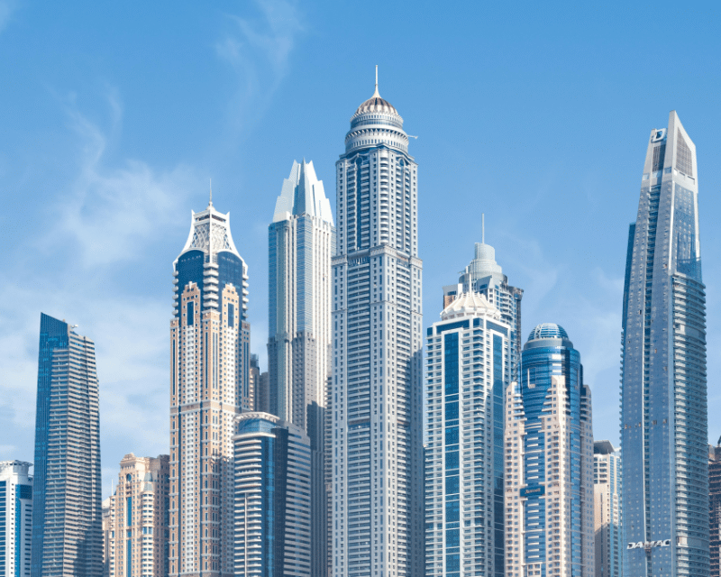 Daytime cityscape of modern skyscrapers with diverse architectural designs against a clear blue sky.