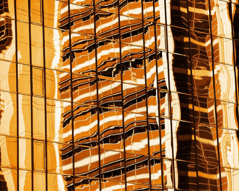 Abstract reflection of a building facade in golden glass panels, creating distorted wave-like patterns.