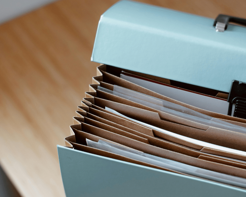 A close-up of an organised accordion file folder filled with neatly arranged documents on a wooden desk.