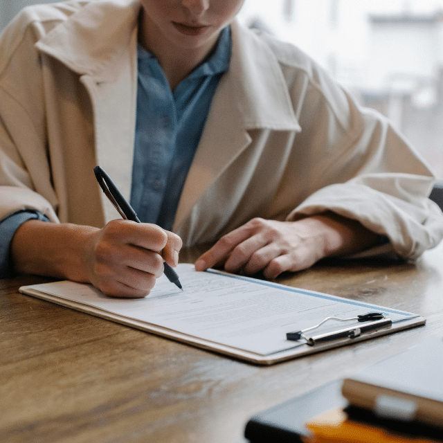 Person writing on a document attached to a clipboard at a desk.
