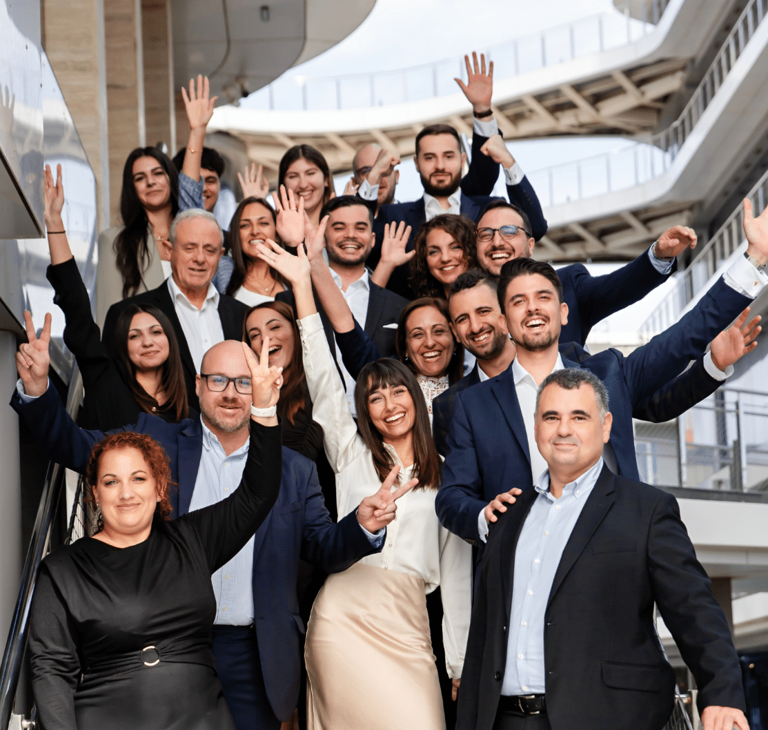 Group photo of the A2CO team standing on stairs outside their offices, smiling and waving at the camera.